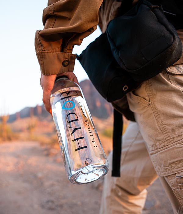 Person exploring the outdoors with a bottle of Hydor cellular hydration water in hand.
